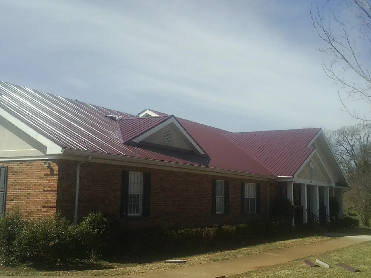 Red metal roof with gabled entries on a long brick building, from a Hail Damage Roof Repair job in Tifton