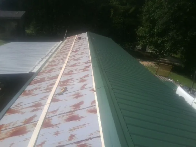 Old rusted panels beside newly installed green metal roofing — Wind Damage Roof Repair by Roofing Brothers in Tifton