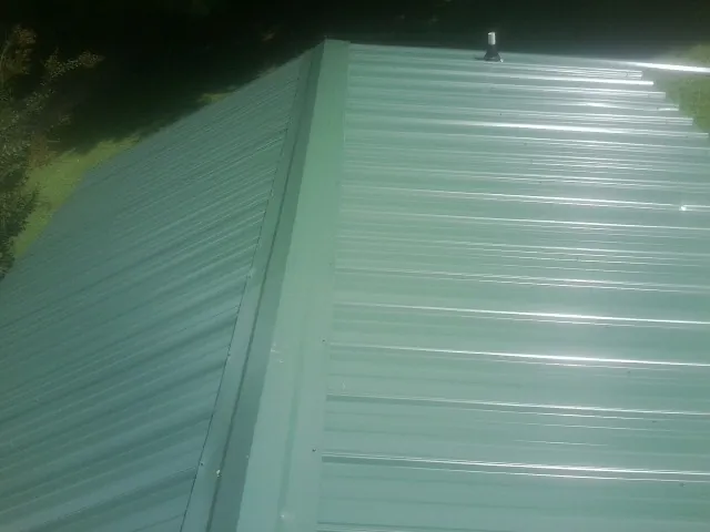 New green metal panels meeting at the ridge of a roof — Flat Roof Repair work by our crew in Tifton