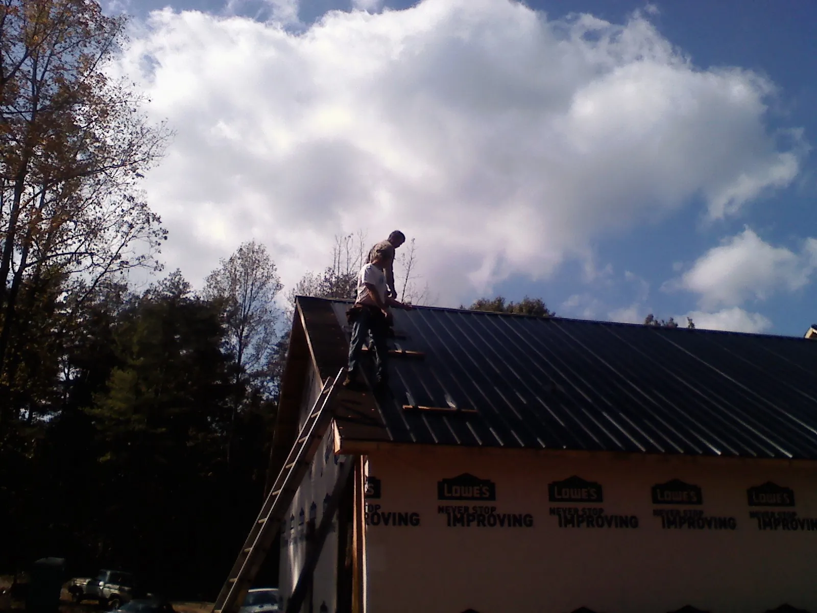 Roofer fastening dark metal panels high against a cloudy sky, from a Roof Inspection job in Tifton