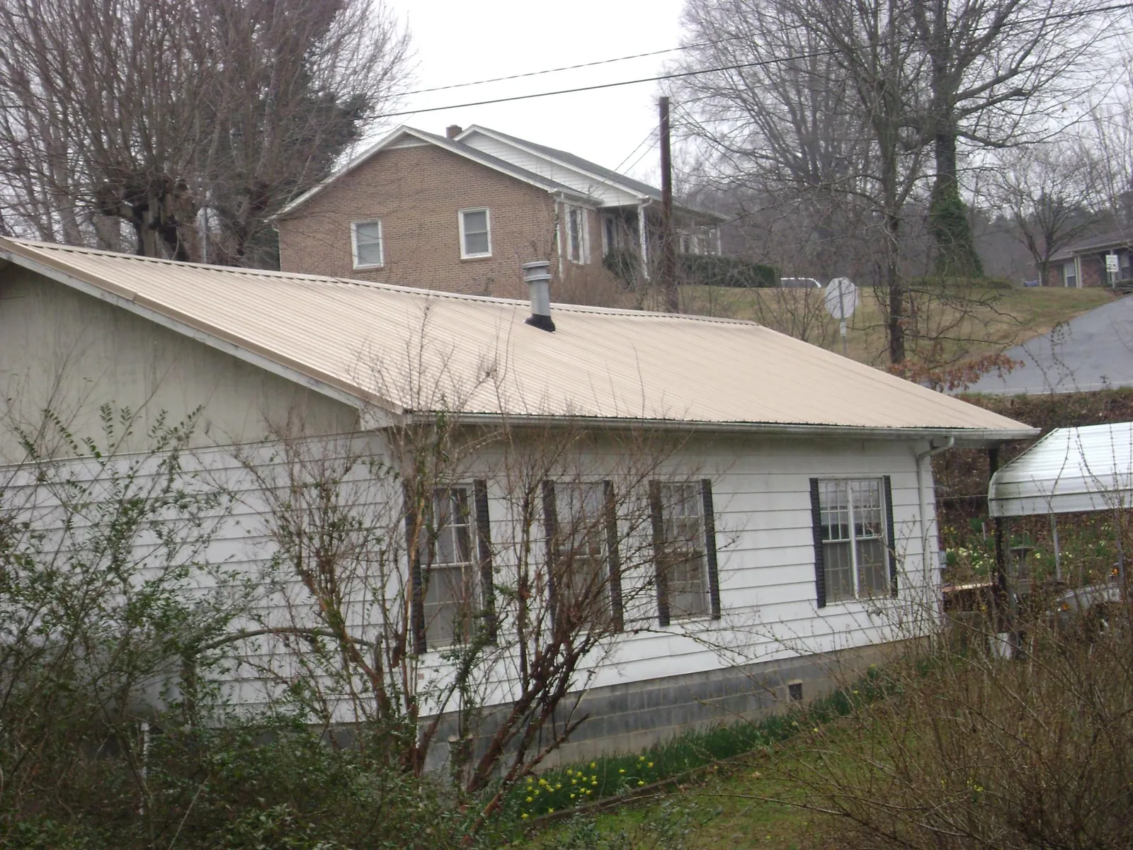 Tan metal roof on a white sided house set into a hillside — Commercial Roofing by Roofing Brothers in Tifton