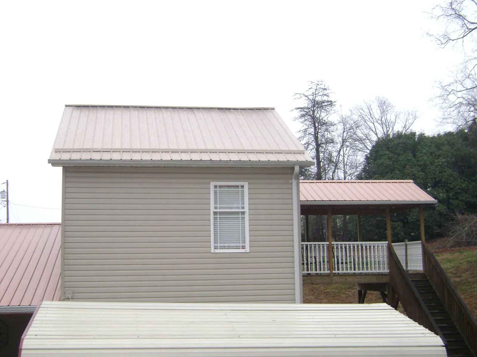 Tan metal roofs on a two story addition and attached porch, from a Roof Replacement job in Tifton