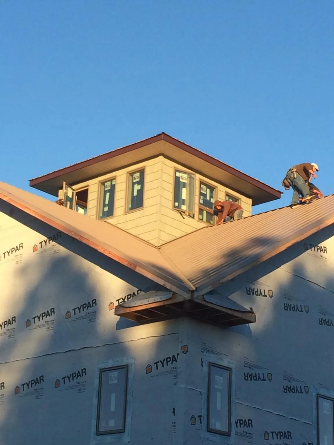Roofers working around a rooftop cupola on a new metal roof at sunset — Roof Waterproofing in Tifton by Roofing Brothers